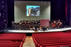Das Orchester spielt nicht direkt auf der Seebühne, sondern im Großen Saal des Festspielhauses mit Videoleinwand auf die Agierenden